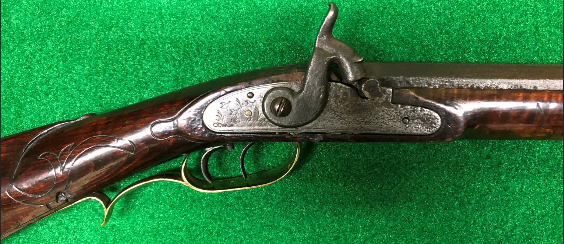 This photo features the lock, wrist carving, and trigger guard areas of an antique black powder rifle built by Daniel Benjamin Troutman, who lived and worked in Bedford and Somerset Counties, Pennsylvania before moving to Kansas.